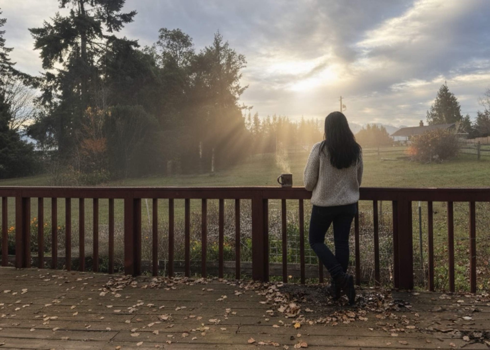Karen on her deck at sunrise, looking out over field and firs